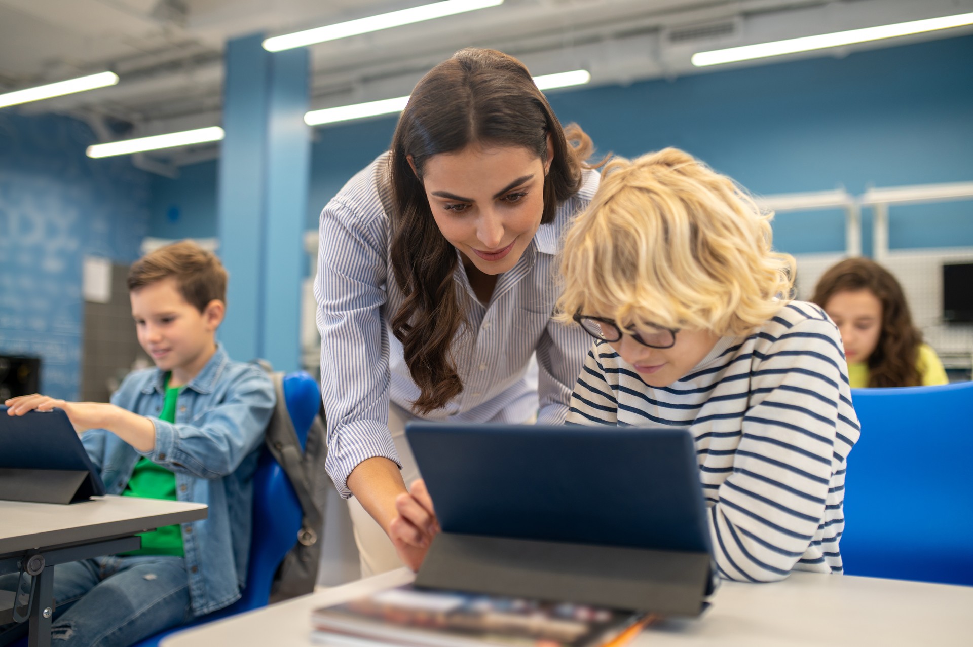 Woman touching tablet screen of boy sitting at desk